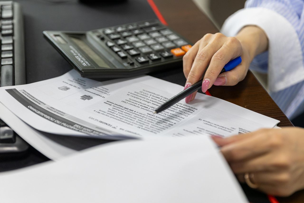 Close-up of a woman's hand reviewing financial documents with a calculator.