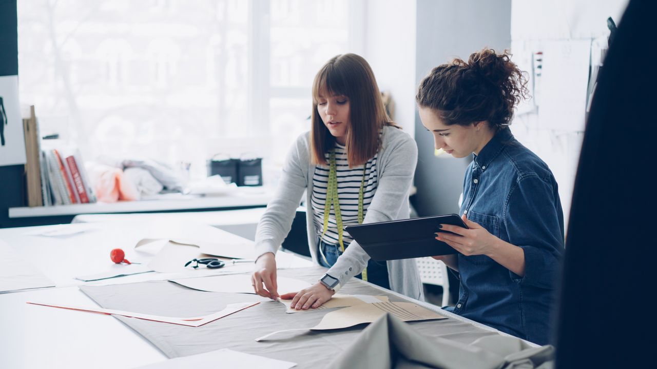 Two women working together on a fashion design project in a bright studio.