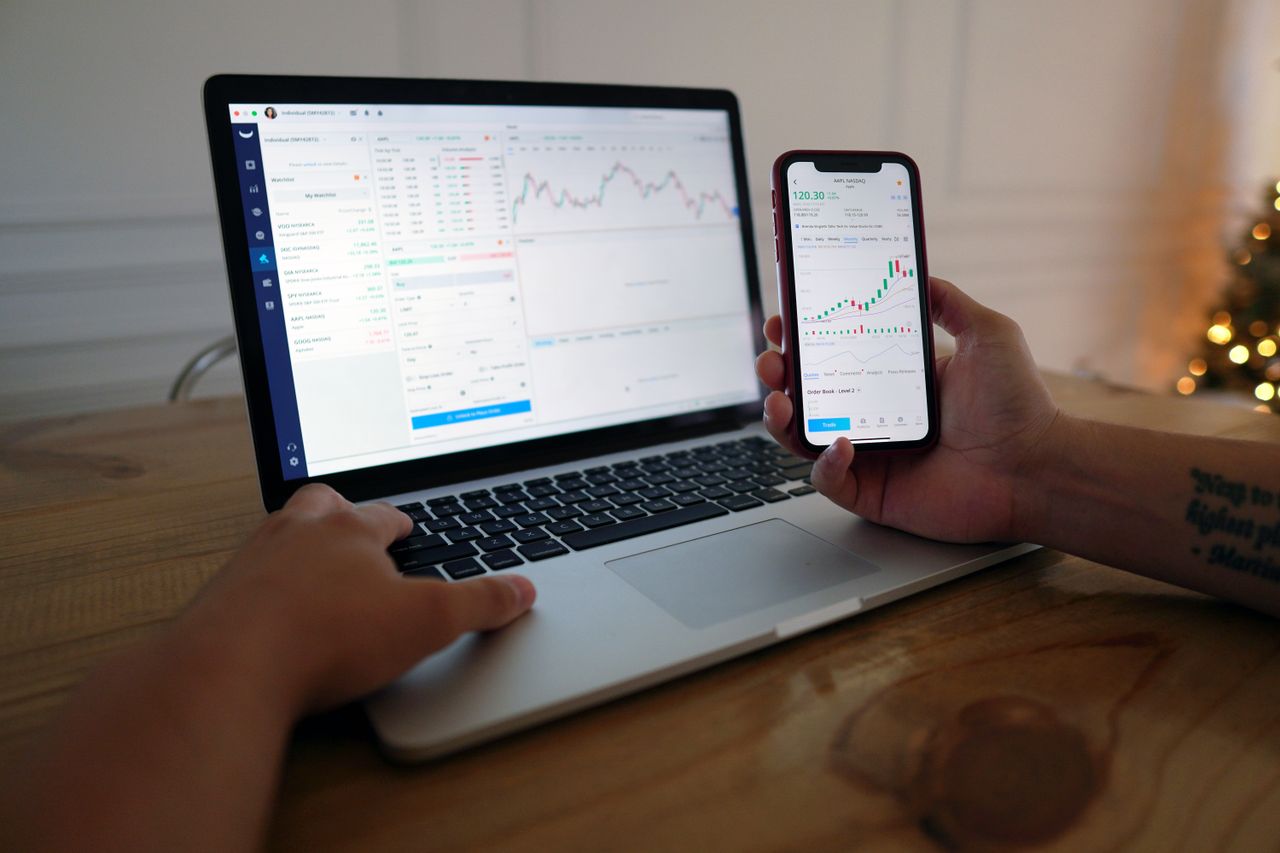 Hands analyzing financial charts on a laptop and smartphone showing market trends.